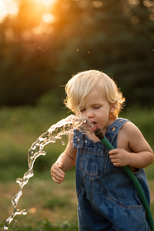 Sample child drinking from water hose in garden