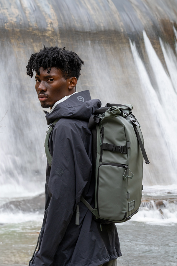 Posing in front of waterfall with a wandrd backpack in green colour